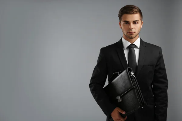 Elegante uomo in completo con valigetta su sfondo grigio — Foto Stock