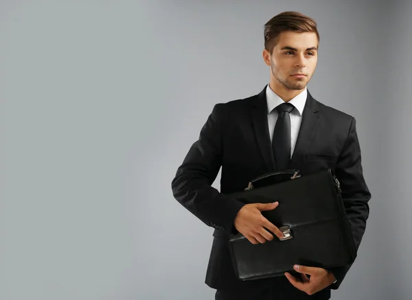 Елегантний чоловік у костюмі з портфелем на сірому фоні — стокове фото