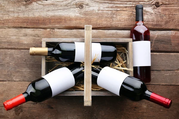 Weinflaschen im Korb auf hölzernem Hintergrund — Stockfoto