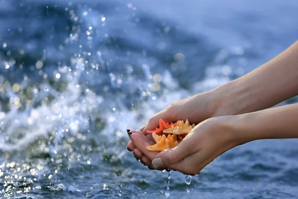 Vrouwelijke handen houden zeesterren en aanraken van water — Stockfoto