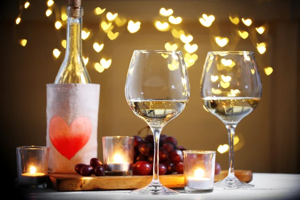 Wine glass near bottle on hearts bokeh background — Stock Photo, Image