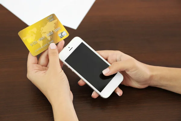 Женщина проверяет баланс счета на смартфоне с помощью мобильного банковского приложения на деревянном фоне — стоковое фото