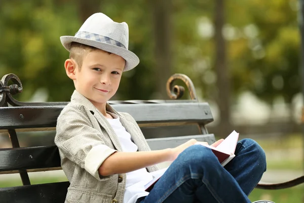 小男孩坐在公园长椅上读书 — 图库照片