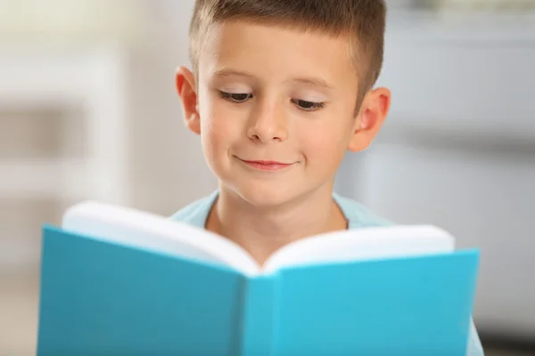 Kleine jongen met boek zittend op tapijt, op huis interieur achtergrond — Stockfoto