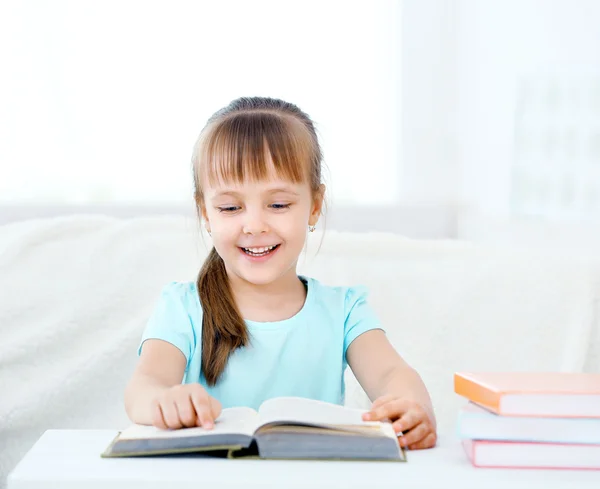 Hermosa niña sentada en el sofá con libro, en el fondo interior de casa —  Fotos de Stock