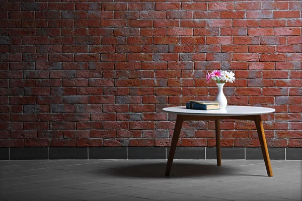 Table with flowers and books on brick wall background — Stock Photo, Image