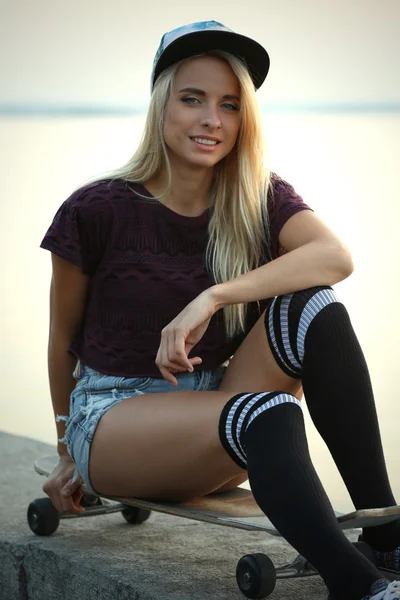 Mujer joven con tabla de patinar en la orilla del río —  Fotos de Stock