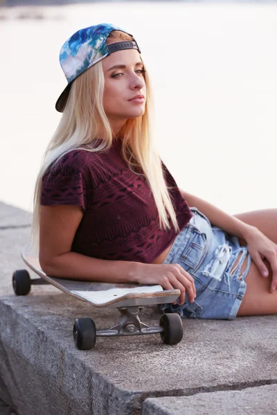 Mujer joven con tabla de patinar en la orilla del río —  Fotos de Stock