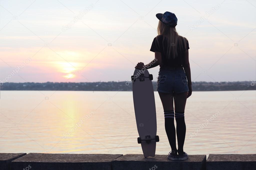 Young woman with skating board on the riverside