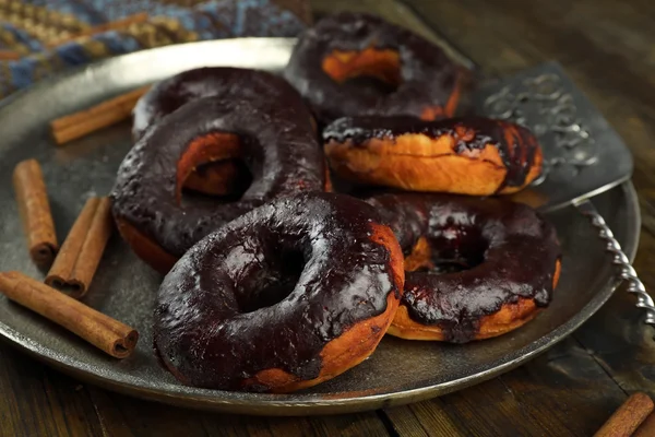 Delicious doughnuts with chocolate icing and cinnamon on metal tray close up — Stock Photo, Image