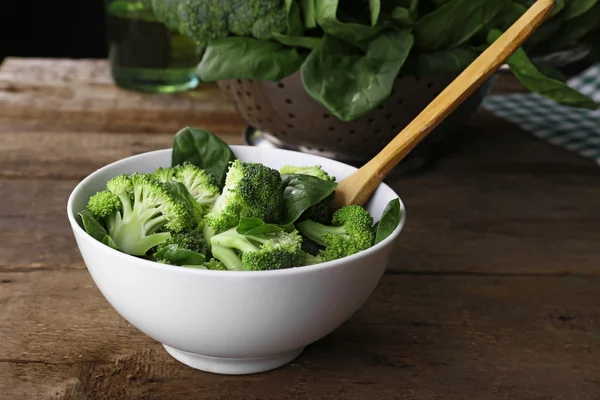 Färsk broccoli med spenat i skål på träbord nära håll — Stockfoto