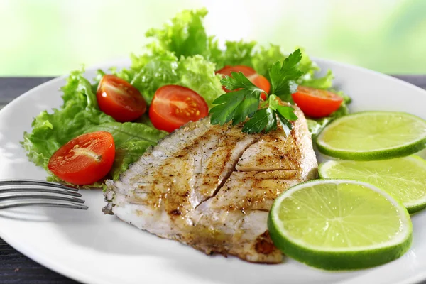 Рыбное филе с салатом и лаймом на тарелке крупным планом — стоковое фото