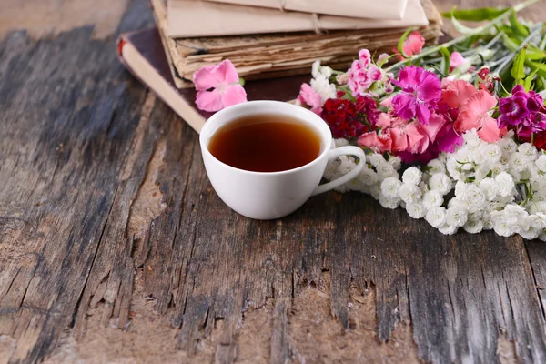 Старые книги с красивыми цветами и чашкой чая на деревянном столе — стоковое фото