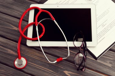 Kırmızı lastik stetoskop ile tablet, gözlük ve ahşap arka plan üzerinde tıbbi geçmişi