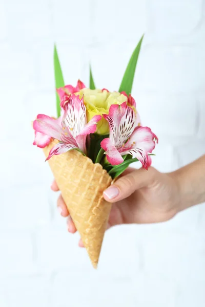 Vrouw hand met wilde bloemen in wafer op lichte muur achtergrond — Stockfoto