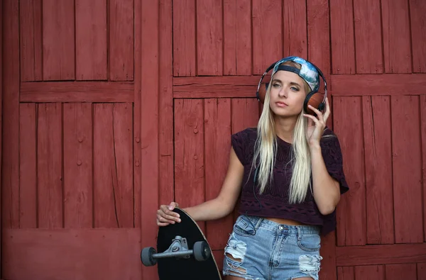 Junge Frau mit Skateboard hört Musik — Stockfoto