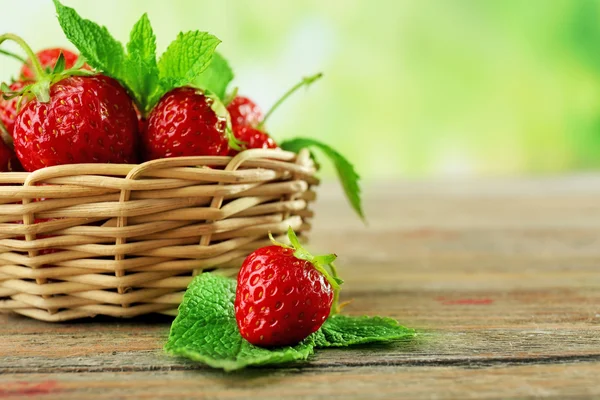 Reife Erdbeeren mit Blättern im Weidenkorb auf Holztisch vor verschwommenem Hintergrund — Stockfoto