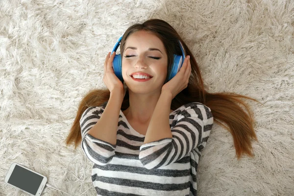 Donna che ascolta musica in cuffia sul tappeto in camera — Foto Stock