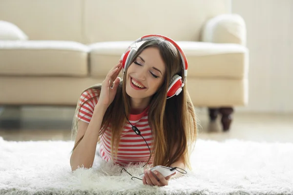 Женщина слушает музыку в наушниках, лежа на ковре в комнате — стоковое фото