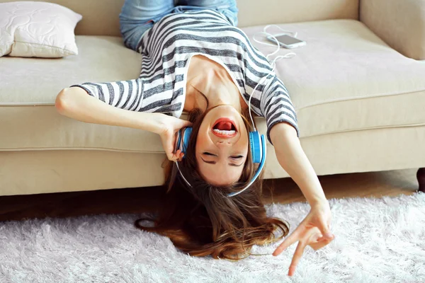 Kvinnan lyssnar musik i hörlurar liggande på soffan i rummet — Stockfoto