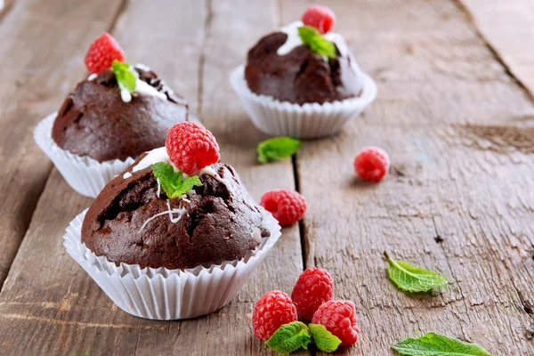 Deliciosos cupcakes de chocolate con bayas y menta fresca en la mesa de madera de cerca —  Fotos de Stock