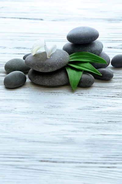 Piedras de spa con flores y hojas verdes sobre fondo de madera — Foto de Stock