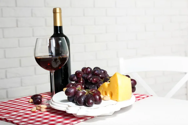 Raisin rouge et fromage avec bouteille de vin en verre sur fond intérieur clair — Photo