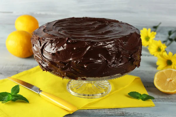 Delicious chocolate cake near lemons on grey wooden table — Stock Photo, Image