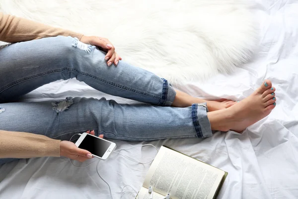 Mulher de jeans azul assistindo telefone na cama ponto de vista superior — Fotografia de Stock