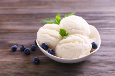 Vanilyalı dondurma ahşap arka plan üzerinde bir yaban mersini ve nane ile dekore edilmiş bir kase