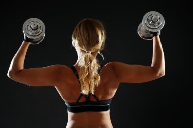 Koyu arka plan üzerinde dumbbells ile atletik kadın