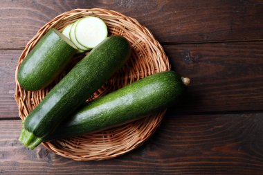 Fresh zucchini on wicker mat on wooden background clipart