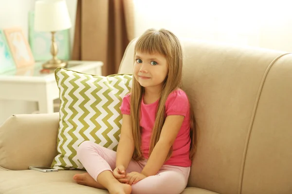 Vacker liten flicka sitter på soffan — Stockfoto