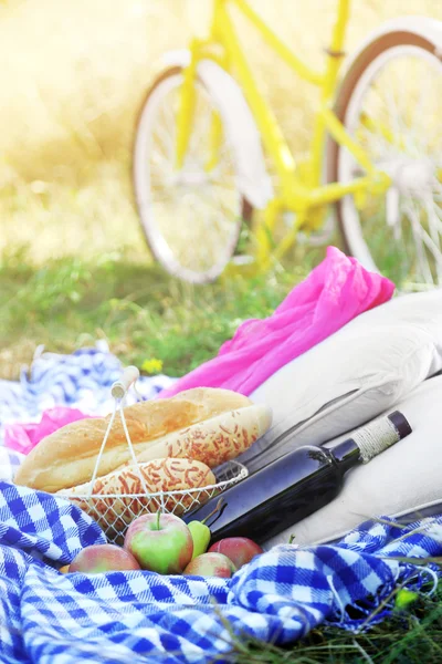 Old yellow bicycle and picnic snack on checkered blanket on grass in park — Stock Photo, Image