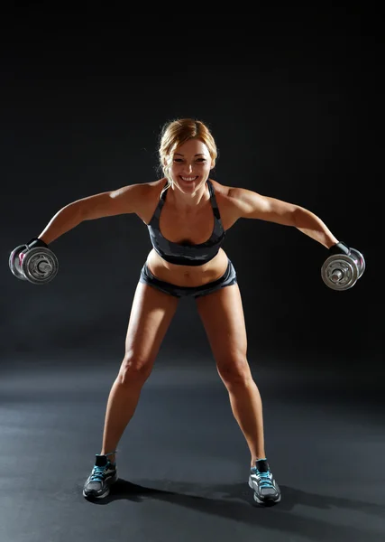 Koyu arka plan üzerinde dumbbells ile atletik kadın — Stok fotoğraf