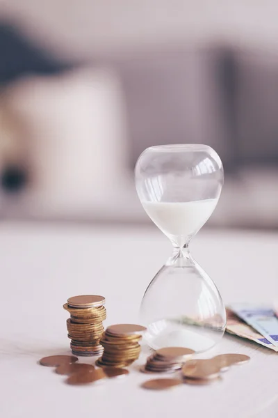 Sanduhr mit Geld auf Tisch auf hellem Hintergrund — Stockfoto