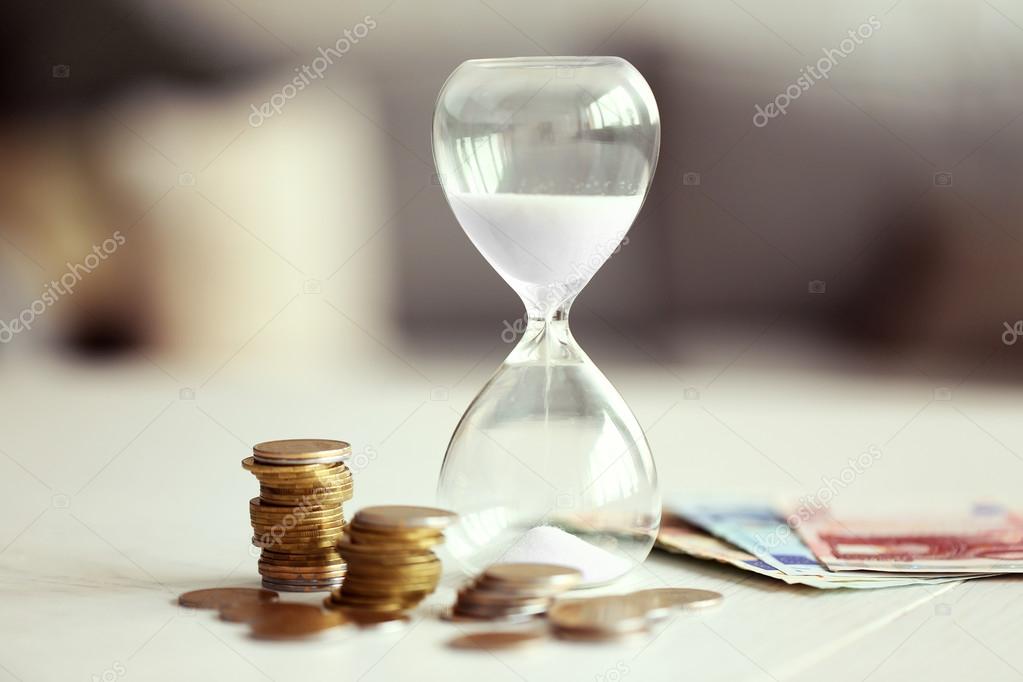 Hourglass with money on table on bright background