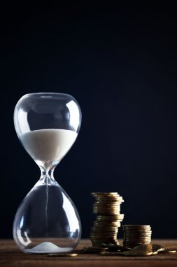 Kum saati ve sikkeler üzerinde siyah arka plan üzerine ahşap masa