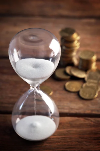 Reloj de arena y monedas en primer plano de mesa de madera —  Fotos de Stock