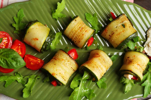 Rotoli di zucchine con formaggio, peperoni e rucola sul piatto, primo piano, sullo sfondo della tavola — Foto Stock