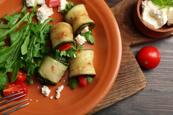 Rotoli di zucchine con formaggio, peperoni e rucola sul piatto, primo piano, sullo sfondo della tavola — Foto Stock