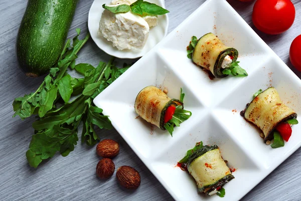 Zucchini rolls with cheese, bell peppers and arugula on plate, close-up, on table background — Stock Photo, Image