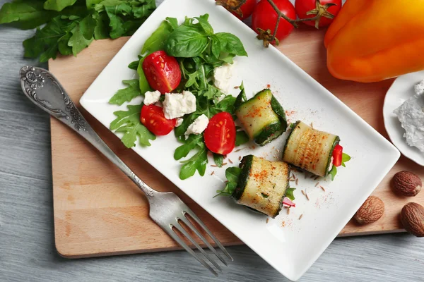 Zucchini rolls with cheese, bell peppers and arugula on plate, close-up, on table background — Stock Photo, Image