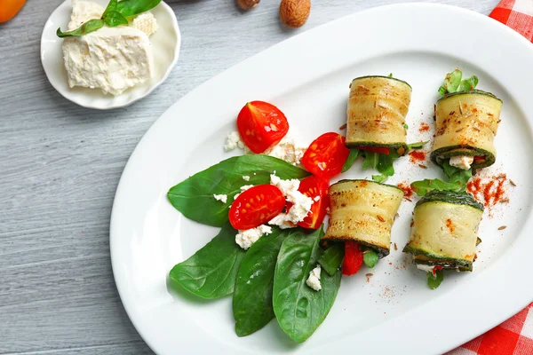 Rotoli di zucchine con formaggio, peperoni e rucola sul piatto, primo piano, sullo sfondo della tavola — Foto Stock