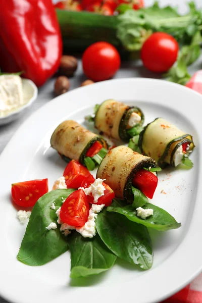 Rotoli di zucchine con formaggio, peperoni e rucola sul piatto, primo piano, sullo sfondo della tavola — Foto Stock