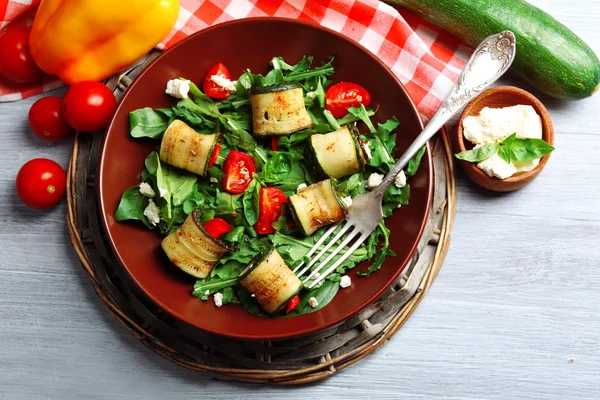 Insalata con rucola e involtini di zucchine su piatto, su fondo tavola — Foto Stock