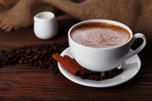 Secangkir kopi dengan krim dan biji kopi dengan latar belakang kayu — Stok Foto