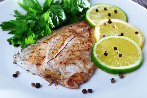 Рыбное филе с зеленью и лаймом на тарелке крупным планом — стоковое фото