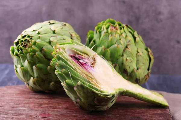 Artichokes on cutting board, on color wooden background — Stock Photo, Image