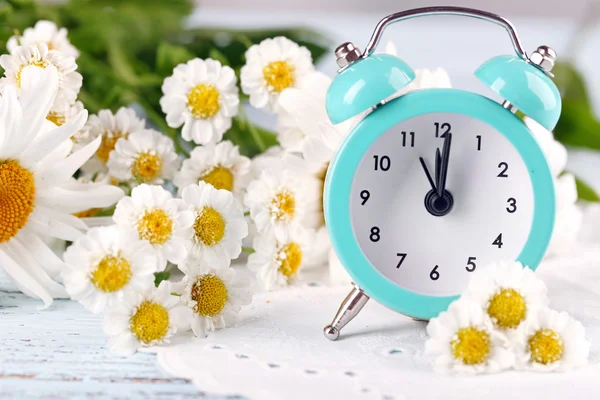 Pequeño despertador con hermosas flores en la mesa de cerca — Foto de Stock